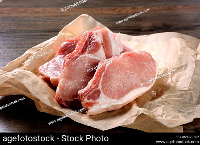 A pile of fresh chopped raw pork steaks over the bones in the wrapping paper on the table. Close-up