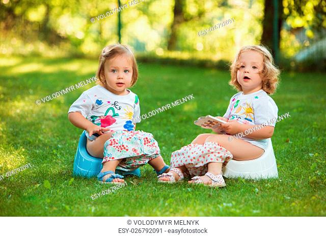 The two little baby girls two-year old sitting on pots against green grass