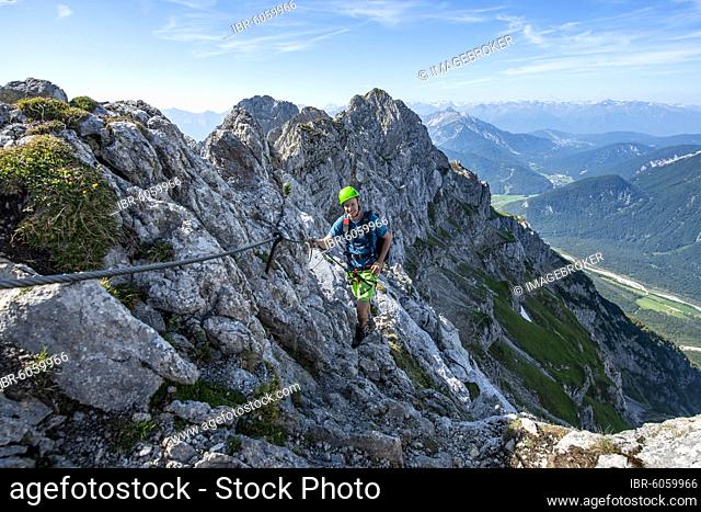 Mountaineer climbs on a secured fixed rope route, Mittenwalder Höhenweg, view into the Isar valley near Mittenwald, Karwendel Mountains, Mittenwald, Bavaria