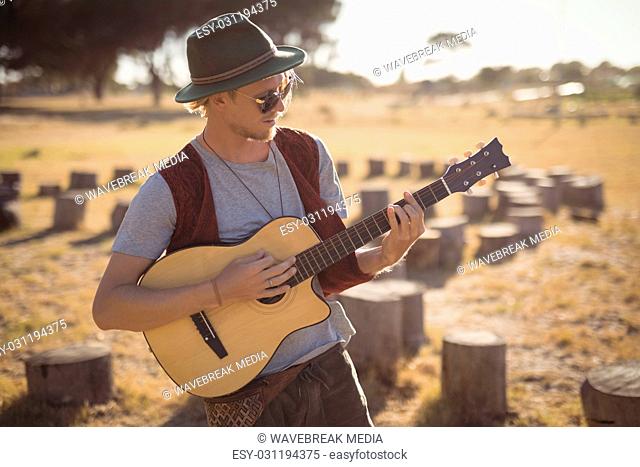 Young man playing guitar while standing on field