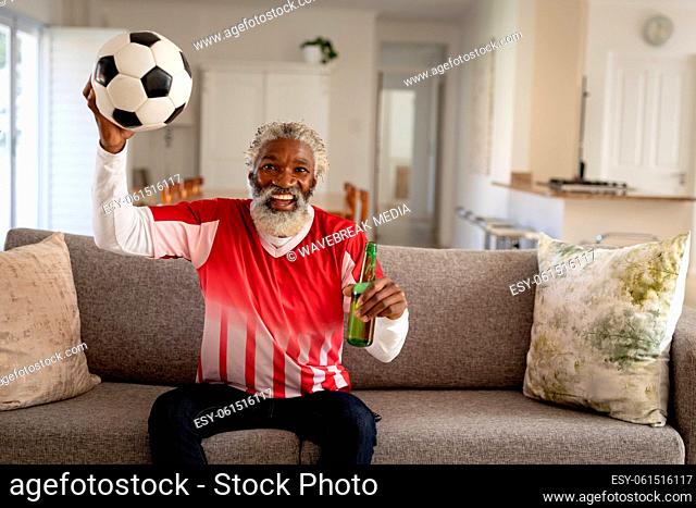 Senior man holding beer bottle and football cheering while watching sports on TV