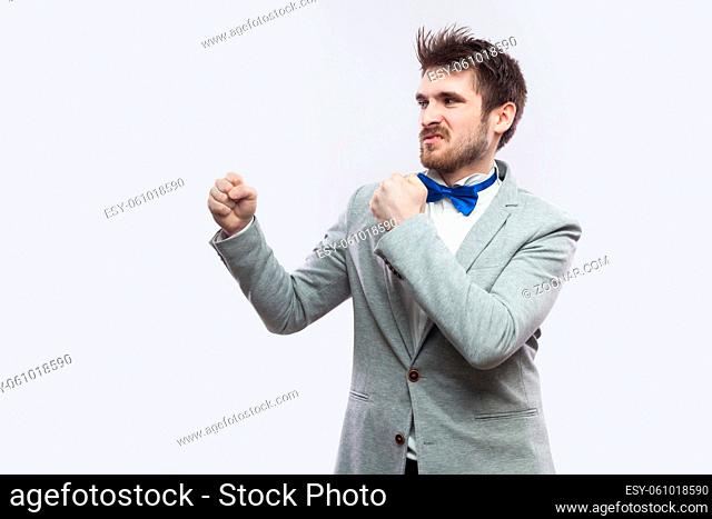 Profile side view portrait of serious handsome bearded man in casual grey suit and blue bow tie standing with boxing fists and looking straight