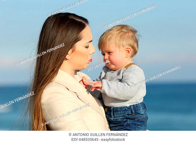 Mother and her angry baby son frowning outdoors on the beach