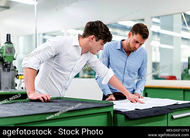 Male colleagues discussing over blueprint in factory