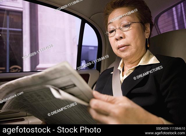 Asian businesswoman reading newspaper in car
