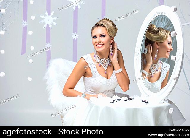 Beautiful young woman with bright purple makeup and fancy hairdo sitting behind mirror table. Gorgeous winter bride. Copy space
