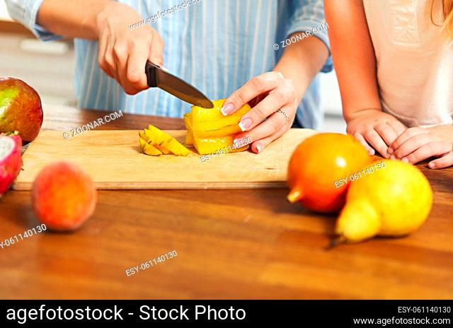 Beautiful little girl with her mother in the kitchen preparing a fresh fruit salad. Close up