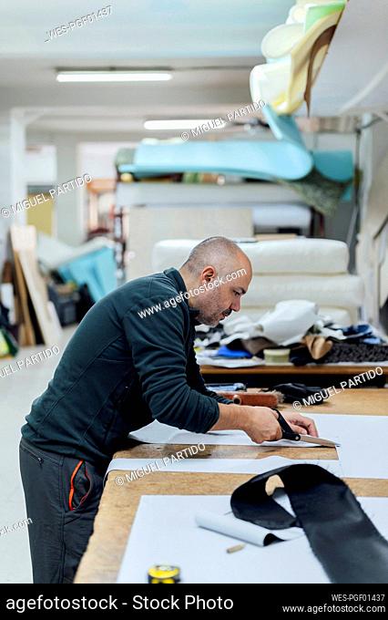 Upholsterer worker cutting fabric at workbench