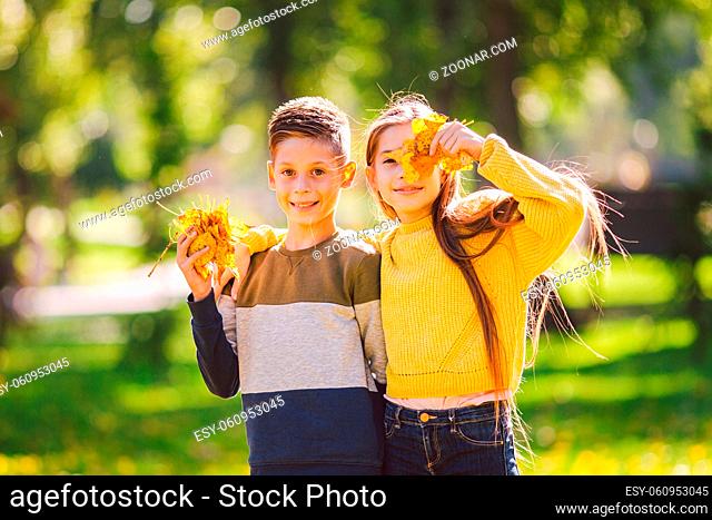 Friendship between siblings. Siblings together outside with bright colored background. Kids autumn portrait. Brother and sister playing in autumn park leaves