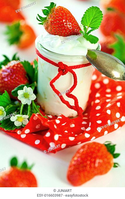 Fresh ripe red farm strawberries with a glass jar of healthy yogurt served on a colorful red country polka dot napkin for a delicious breakfast or appetizer