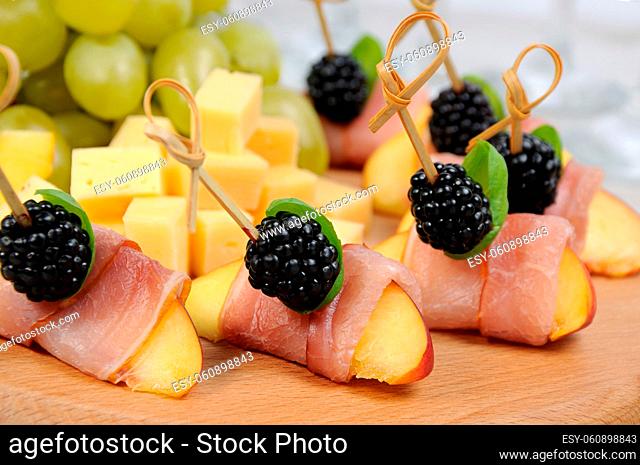 Canape from peach with dried ham and blackberries