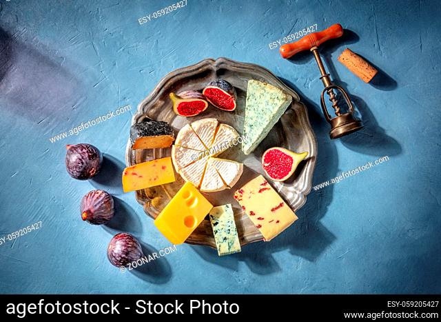 Cheese and wine. A cheeseboard with Brie, blue cheese and other sorts, with a corkscrew and a cork, and a shadow of a glass of red wine, overhead flat lay shot