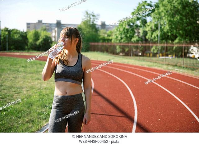 Sportswoman drinking water on racetrack