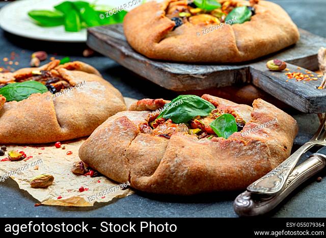 Open pies (galette) with chicken, onion and mushrooms served with green spinach and pistachios, selective focus