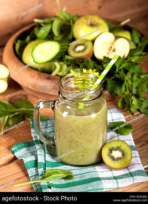 Freshly blended green smoothie in glass jar with straw on wooden background