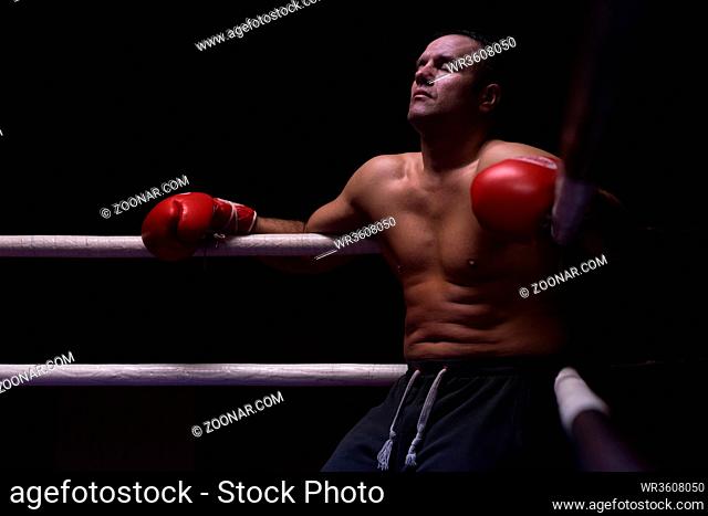 muscular professional kick boxer resting on the ropes in the corner of the ring while training for the next match