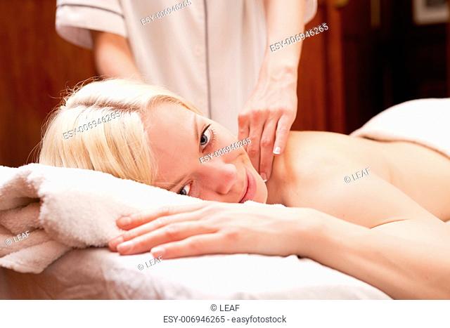 A happy blond woman looking at the camera receiving a shoulder massage