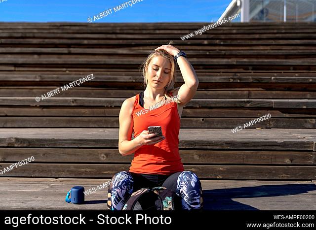 Young woman with head in hand using smart phone while sitting on pier during sunny day