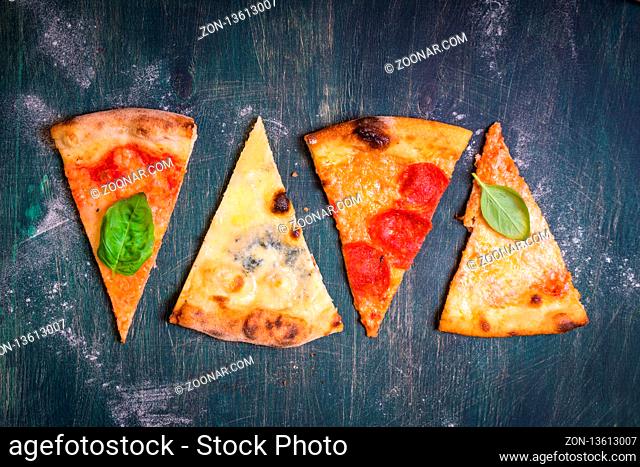 Assorted pizza slices. Margherita, pepperoni, four cheese pizza. Top view. Different types of pizza on the textured old wooden table