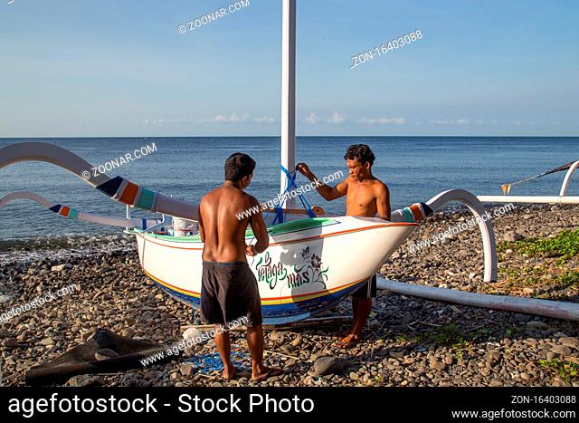 Bali, Indonesia - July 06, 2015: Two fishermen preparing their traditional fishing boats on a beach close to Amed