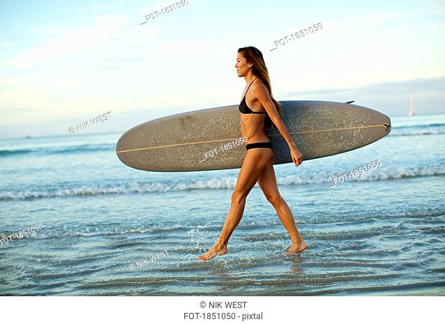 Female surfer carrying surfboard in ocean surf