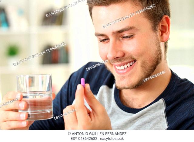 Happy man ready to take a capsule sitting on a sofa in the living room in a house interior