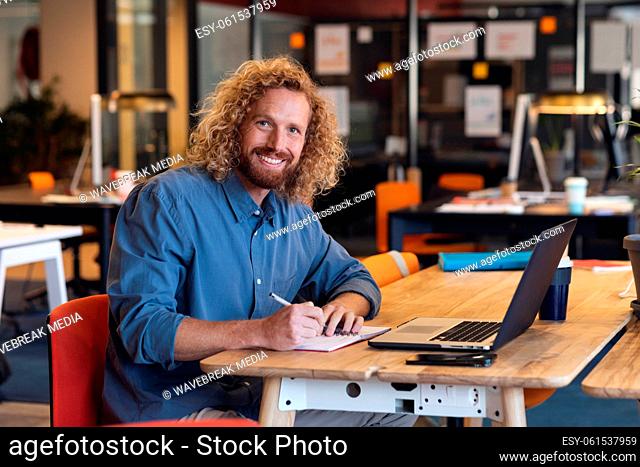 Portrait of young caucasian businessman writing in diary at desk in creative office