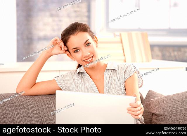Young attractive woman using laptop at home, browsing internet, sitting on sofa, smiling