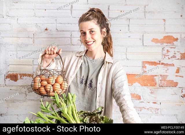Happy grocer holding eggs in front of brick wall