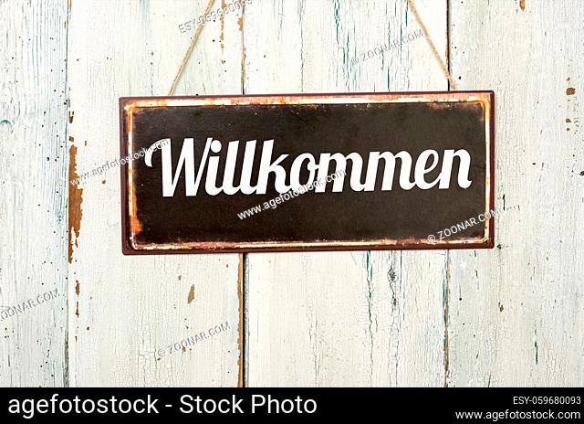 Old metal sign in front of a white wooden wall - German word for Welcome- Willkommen