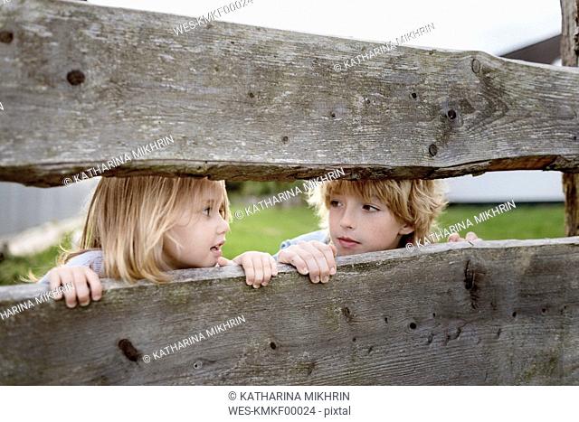Brother and his little sister behind wooden fence