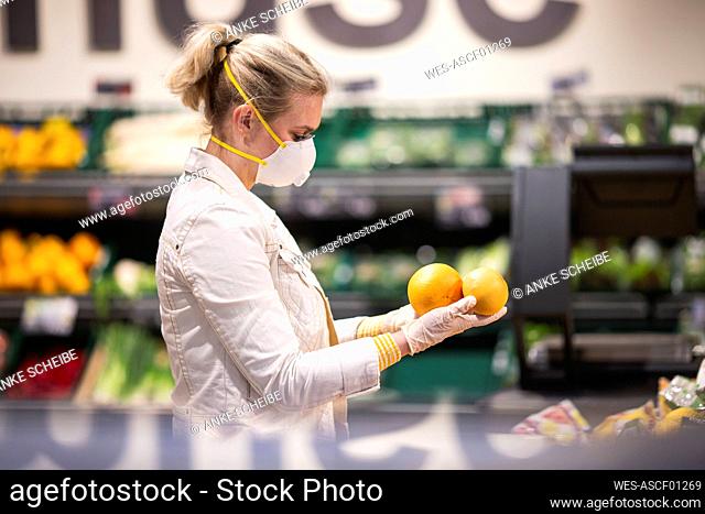 Teenage girl wearing protectice mask and gloves choosing fruits at supermarket