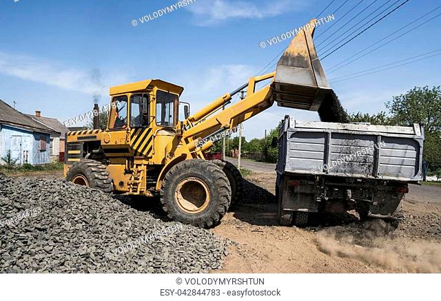 Yellow loader delivering stone gravel into truck during road construction works. The stones for the road. Unloading stone