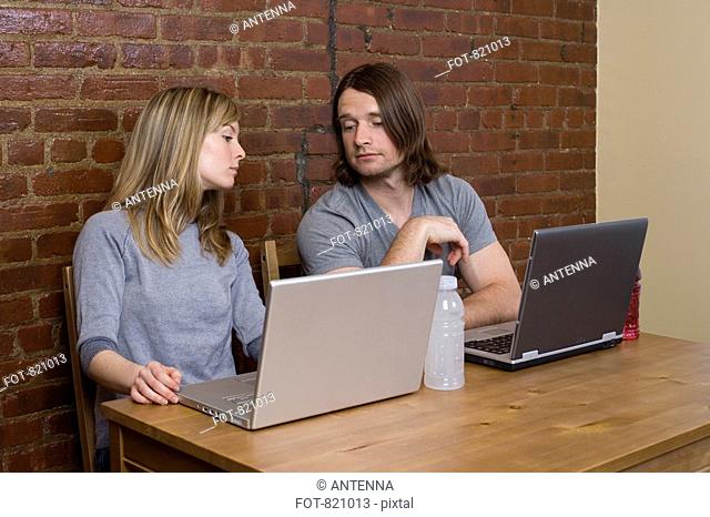 A young couple sitting side by side using laptops