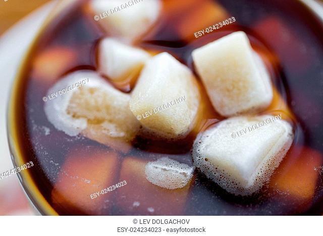 unhealthy eating, object and drinks concept - close up of lump sugar heap drowned in cup of coffee or tea
