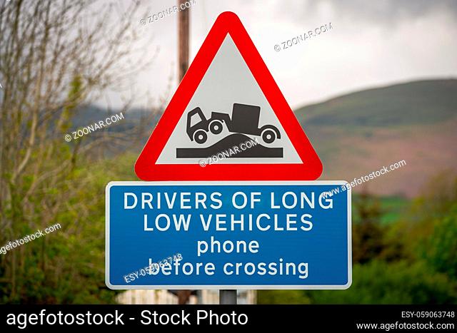 Sign: Drivers of long low vehicles phone before crossing, with blurry background. Seen in Green Road near Strands, Cumbria, England, UK