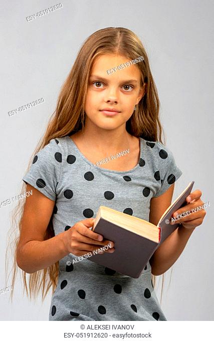 Beautiful ten year old girl reads a book and looks into the frame