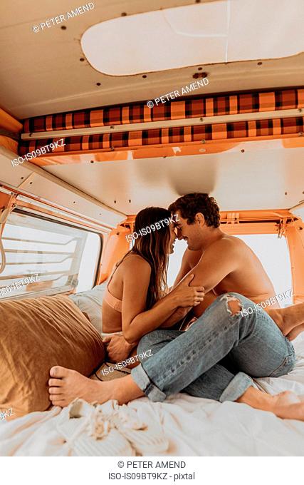 Young surfing couple face to face in back of recreational vehicle at beach, Jalama, California, USA