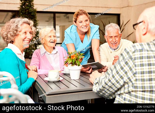 Gruppe Senioren und Pflegekraft mit Tablet Computer beim Kaffee trinken