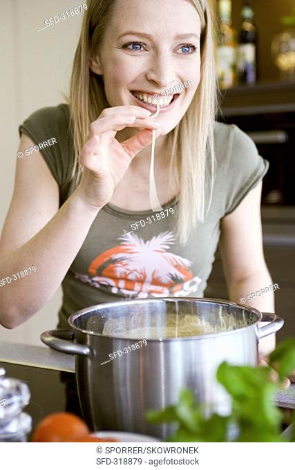 Young woman testing a strand of cooked spaghetti