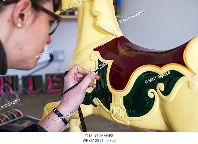 Close up of woman in workshop, painting traditional wooden carousel horse from merry-go-round