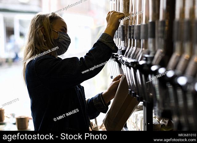 Young blond woman wearing face mask, shopping in waste free wholefood store