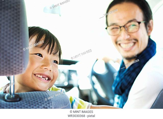 Man wearing glasses and boy sitting in a car, smiling at camera