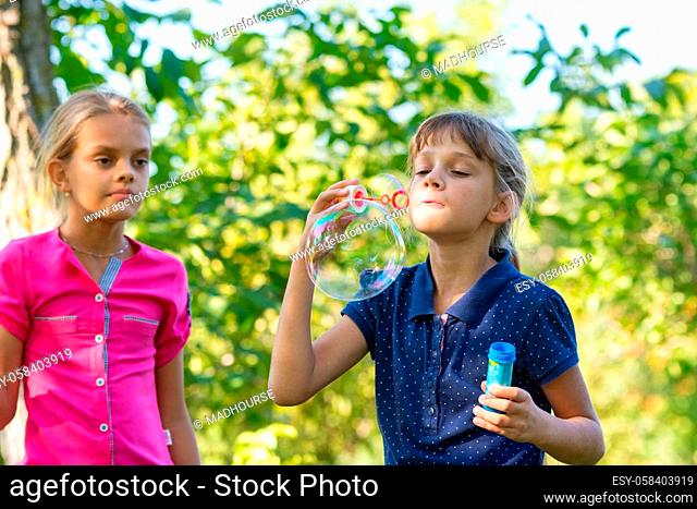 A girl blows bubbles, another girl watches her closely
