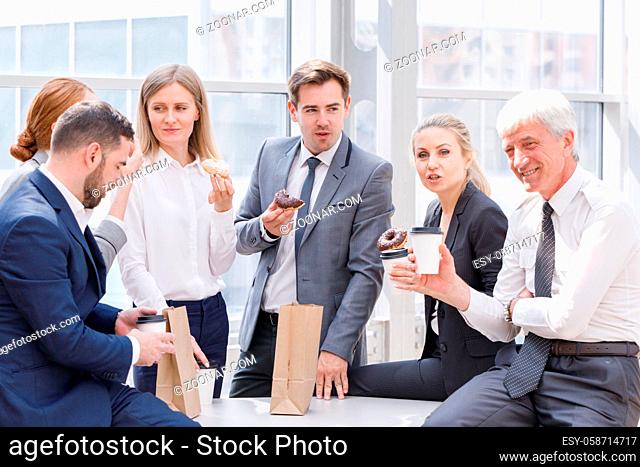 Business people having coffee break eating donuts together in office