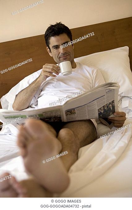 Man reading newspaper in bed