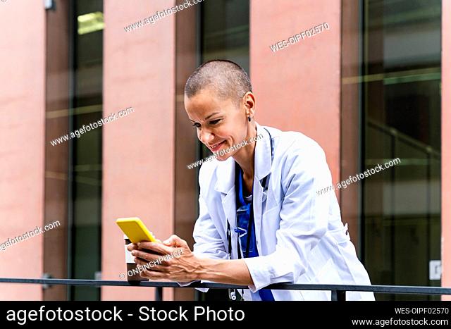 Smiling mature doctor using mobile phone outside hospital