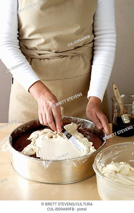 Woman making chocolate cake, spreading cream