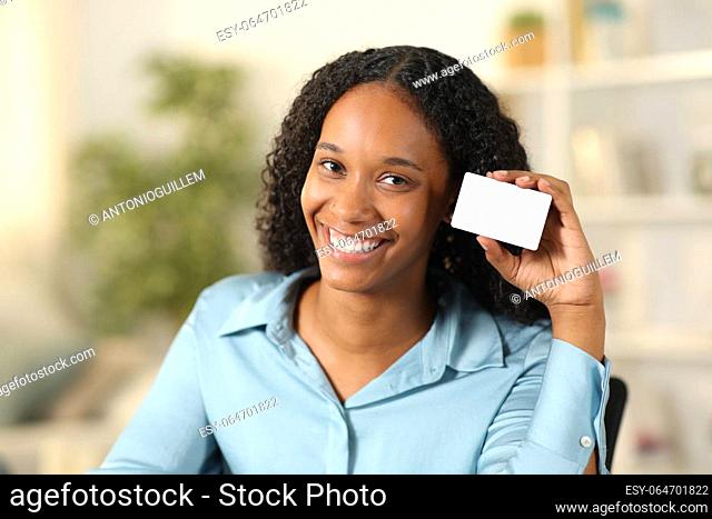 Happy black woman showing blank credit card at home