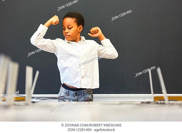 Afrikanischer Junge als Schüler posiert mit geballten Fäusten vor der leeren Tafel